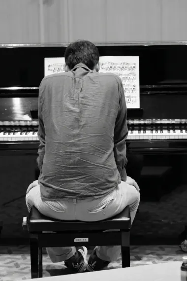 Un adulte de dos, assis à son piano devant une partition, arrêté au milieu du morceau